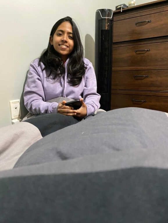 Vinaya Annu sits on the floor in her small bedroom and talks to her roommate