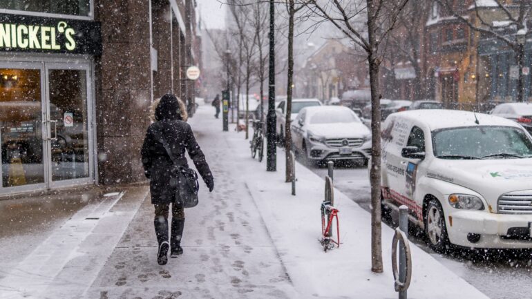 Someone walking down a snow-lined Toronto street in winter wear.