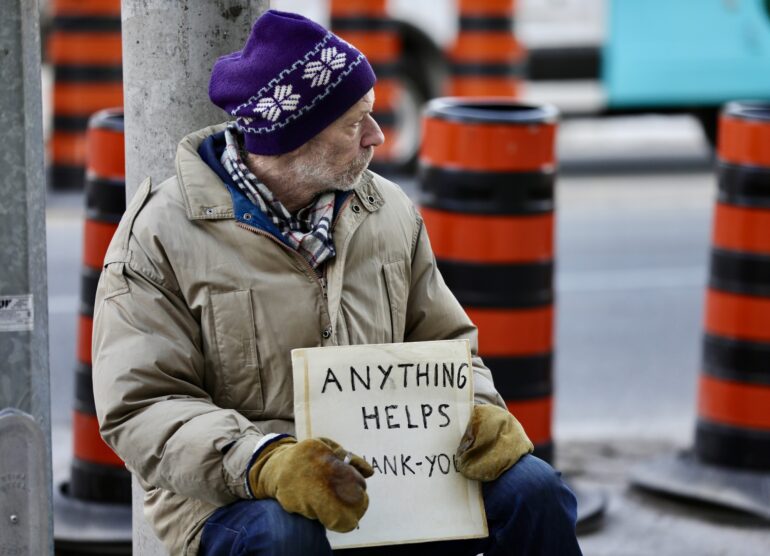 A homeless man is holding a sign on Yonge Street.
