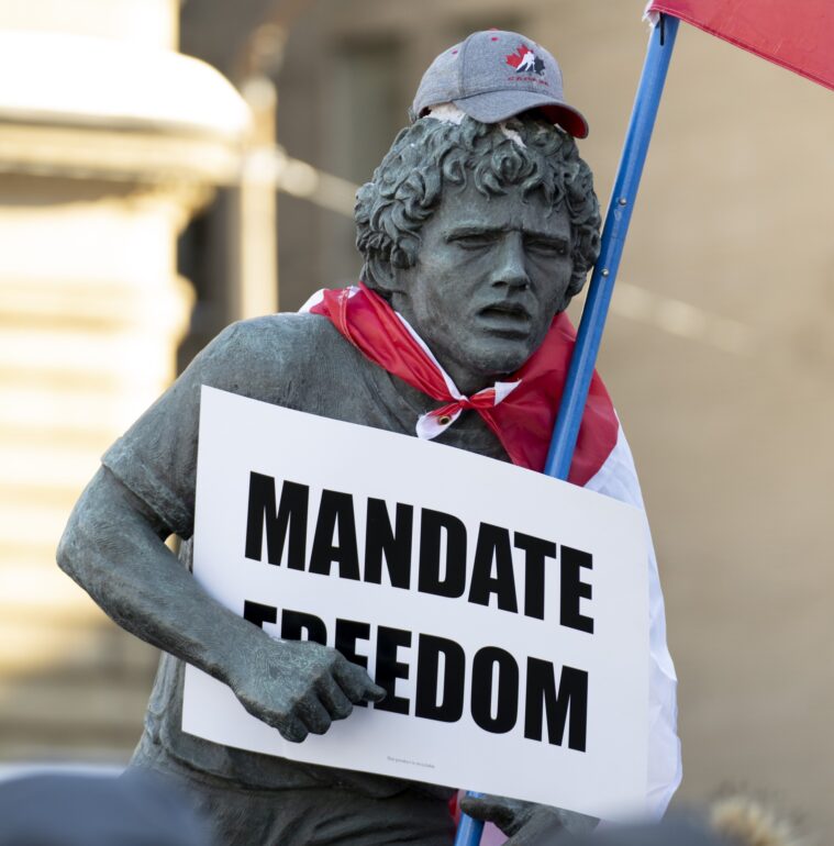 A statue of Terry Fox is decorated with a Canadian flag, protest sign and hat as protesters participating in a cross-country truck convoy protesting measures taken by authorities to curb the spread of COVID-19 and vaccine mandates walk gather Parliament Hill in Ottawa on Saturday, Jan. 29, 2022.