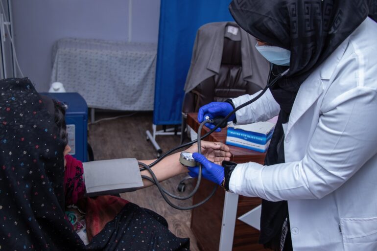 An examination room in an orthopedic ward for women in a health clinic supported by the UN in Hirat, Afghanistan. A  female doctor examines a woman's arm with a stethoscope and another instrument.