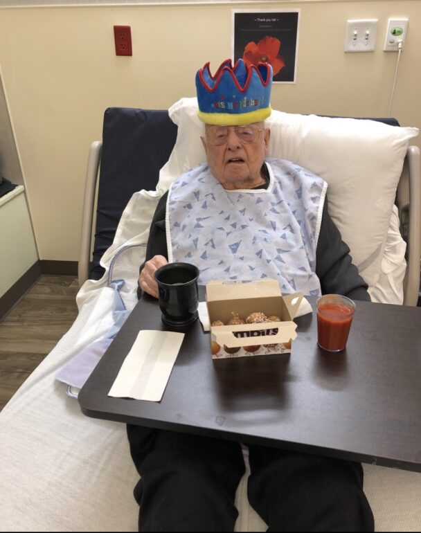 An elderly man sits with a birthday crown and timbits.
