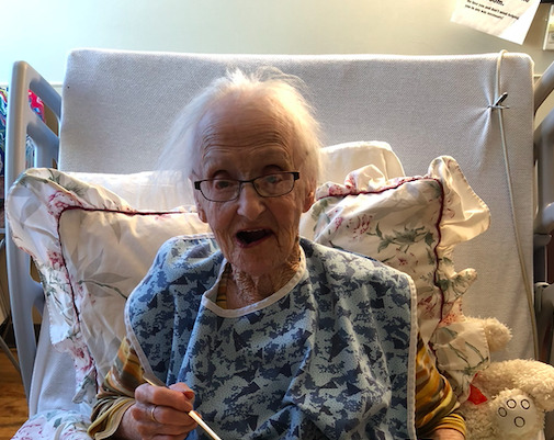 An elderly lady is sitting in a bed, enjoying a meal.