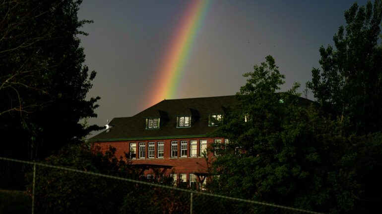 A rainbow is seen in the distance behind the former Kamloops Indian Residential School after a day-long ceremony to mark the first anniversary of the Tk'emlups te Secwepemc announcement of the detection of the remains of 215 children at an unmarked burial site at the former residential school, in Kamloops, B.C., on  May 23, 2022.