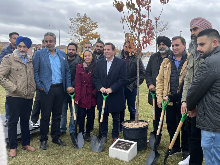 Mayor of Brampton, the regional councillor and the singer's friends standing near the tree holding shovels.