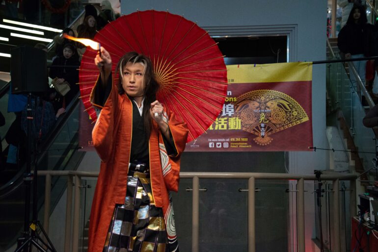 Hayato Kobayashi lights a match while holding an umbrella in a traditional Japanese costume.