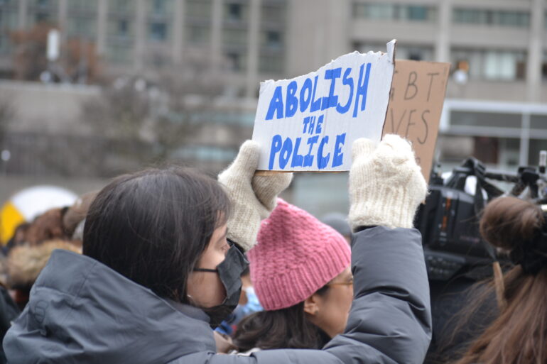 A woman holds a sign at a protest to defund the police.
