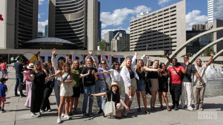 A group of students from Humbers global summer school stand at Nathan Philips park in front of the Toronto sign.