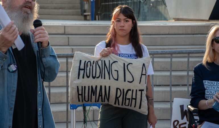 Megan Kee holds a pillow that says "housing is a human right" during a speech.