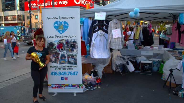 Graciela Lopez standing in front of her vendor tent, with a banner for her foundation Gaucha Argentina -  Love for Humanity.