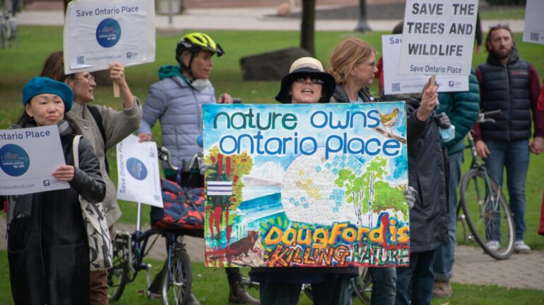Person holding a painted sign that read "nature owns ontario place."