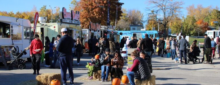 A line of different food vendors in the background and families scattered around at Halloween Food Truck Festival.