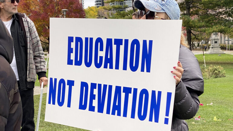 A protest sign reading "education not deviation!" in all caps