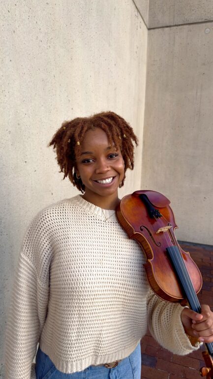 Rachel "Ray" McFarlane smiling, holding up her violin on Nov.22, 2023 in Boston, MA.