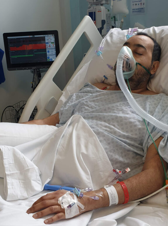 A person lying down on a hospital bed with an oxygen mask on.