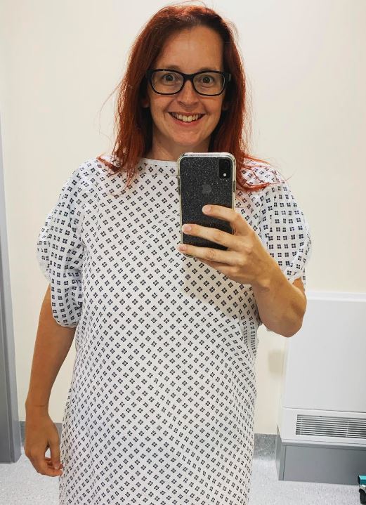 A person in a hospital gown takes a photo in the mirror of themselves.