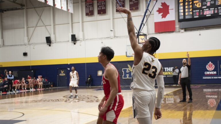 Humber basketball player Jalen Menzies, wearing a white basketball jersey wearing number 23. He just shot the basketball and his follow-through of his jump shot is on screen.