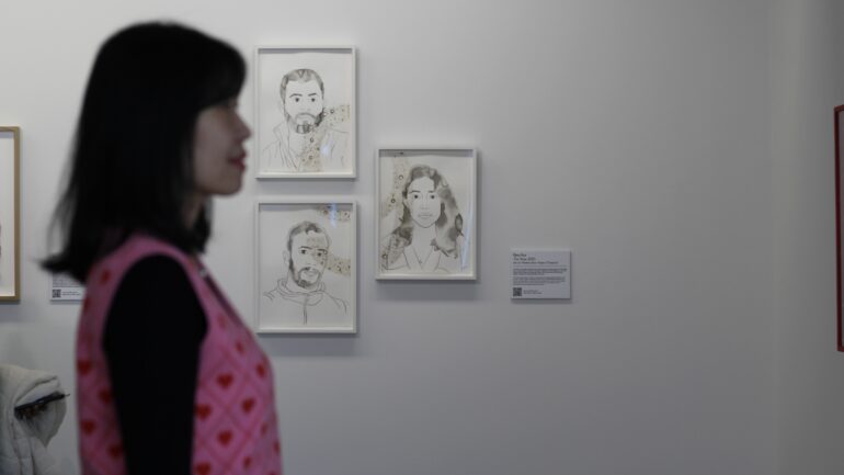 A visitor, Hui Ding is looking at the paintings in the exhibition, Facing Future against the backdrop of Ebru Kru's artwork.
