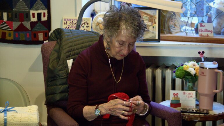 Peggy Goodman knitting at the Spin Me A Yarn store. The items she knits are given away to those who need them to stay warm.