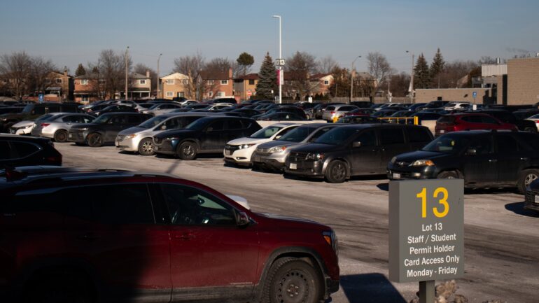 Parking lot filled with cars, a sign reads, "Lot 13 Staff/Student Permit Holder Card Access Only Monday - Friday".