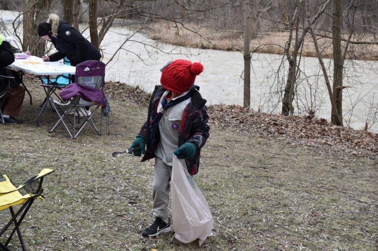 A youngster with a plastic bag and a trash grabber waiting for his mom to start the clean up.