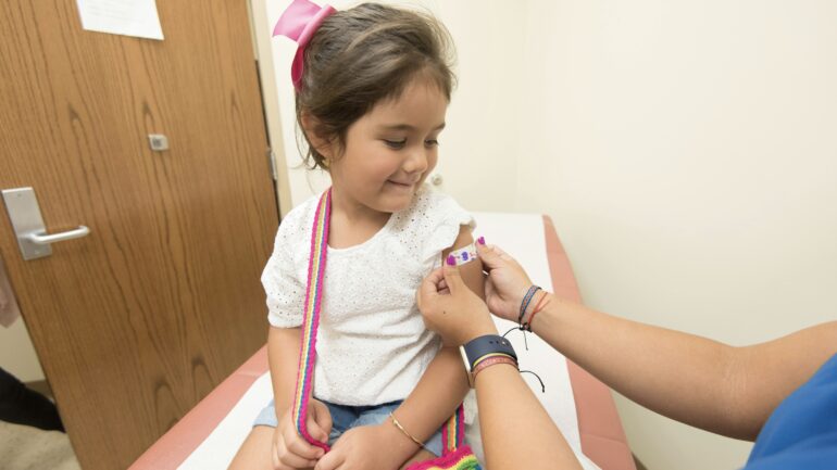 A small girl getting vaccinated in her arm by a nurse.