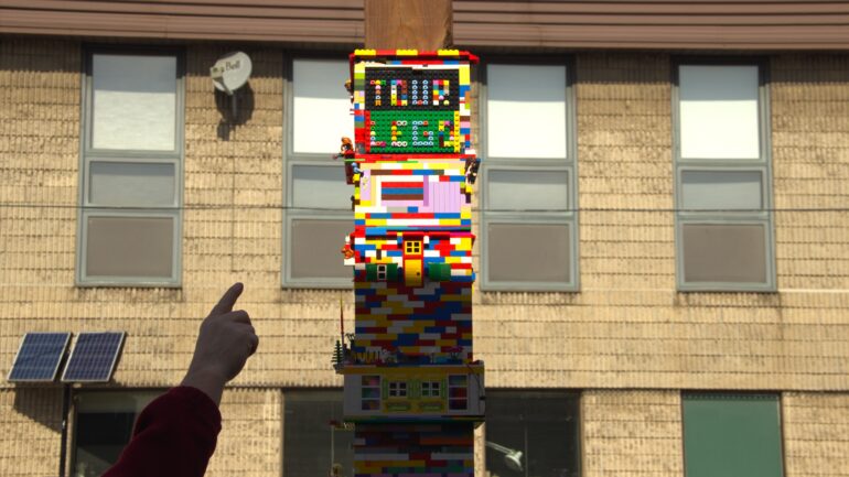 An onlooker pointing at a tower made of Lego toys.