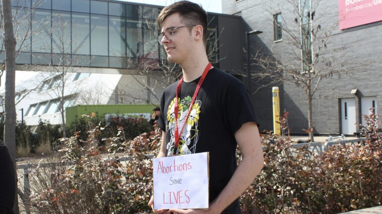 A student held one of Eleanor Drobet's plcard stating, Abortion Saves Lives near the college entrance on Tuesday.