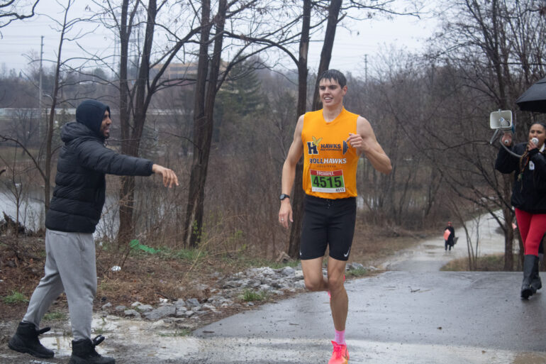 Blaise Uglow runs in the rain with two people egging him on in the background
