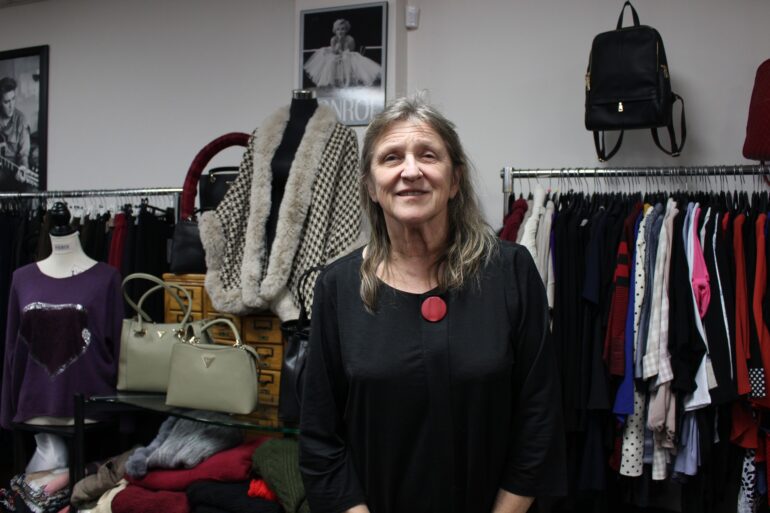 A woman in a black shirt with a red accessory pinned to the collar of her blouse standing in front of merchandise in a store.