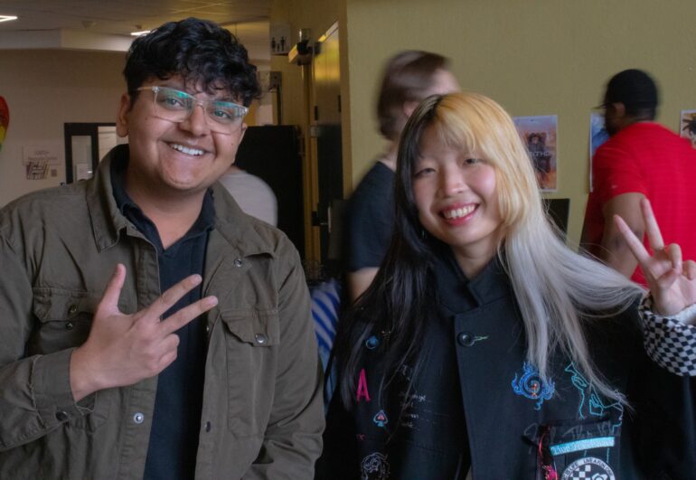 A man on the the left and a woman on the right hold up peace signs to the camera.