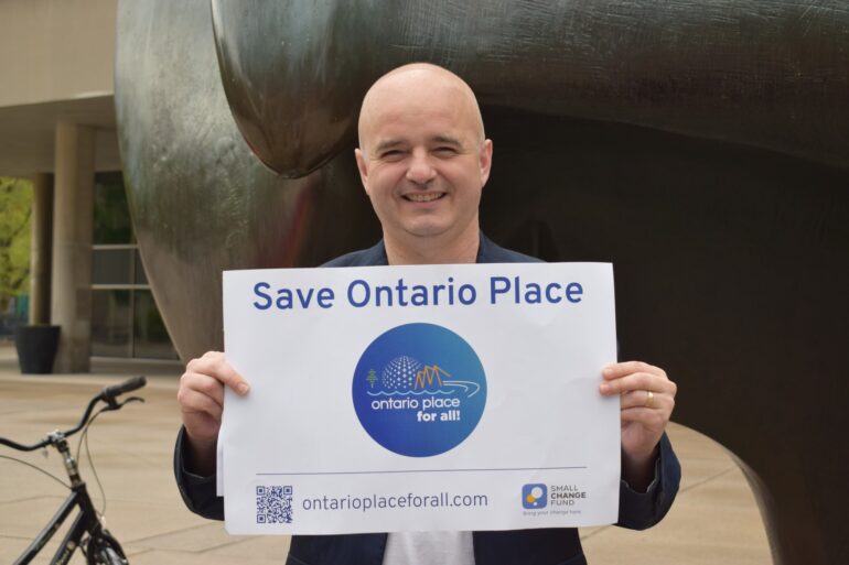 A photo of Ontario Place 4 All Co-chair Norm Di Pasquale holding up a sign at City Hall that reads "Save Ontario Place".