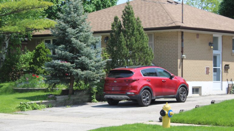 A red hatchback car parked on a street in the afternoon in an Etobicoke neighbourhood.