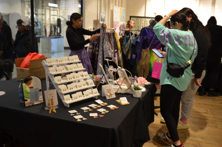 Women standing at booth looking at jewelry and clothing.