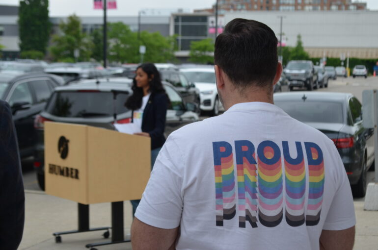 A person wearing a t-shirt with "proud" in colourful letters on the back of the shirt.