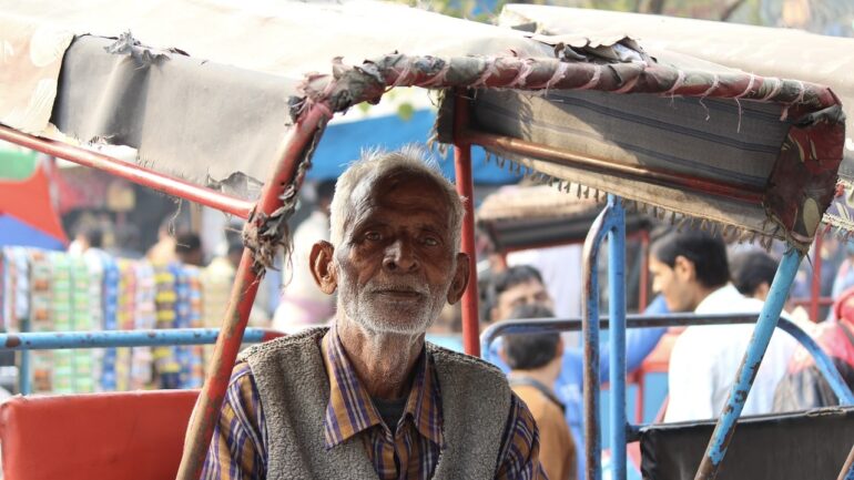 An old rickshaw puller in his rickshaw. Rickshaw is three wheeler with traditionally two person-seating. It is rode like a cycle by the rickshaw puller. It is a common means of public transport.